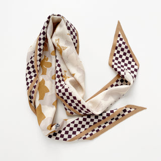 Beige cashmere silk scarf with Art Deco gold bird motifs, bordered by deep brown and cream checkerboard pattern, elegantly draped on white background