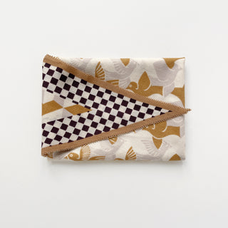Folded beige cashmere silk scarf with Art Deco stylized golden bird motifs and deep brown checkerboard pattern with tan border
