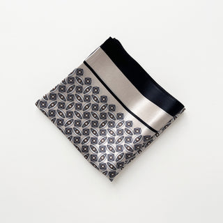 Folded silk bandana scarf with silver-gray background featuring black geometric pattern and solid black border, displayed on white surface