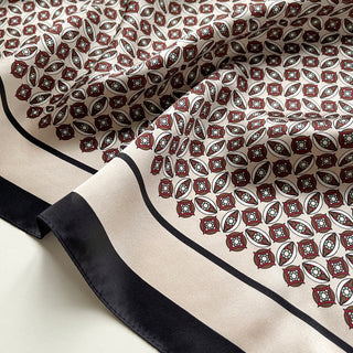 Close-up of silk bandana scarf with red and black heritage geometric pattern, featuring diamond motifs with light blue accents on cream background and black border