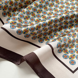 Silk bandana scarf with colorful geometric pattern featuring yellow, blue, and red floral motifs on cream background with brown border trim