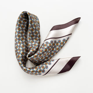 Silk bandana scarf with colorful geometric pattern featuring red, blue, and yellow motifs against white background with burgundy and cream border