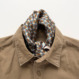 Silk bandana scarf with colorful geometric pattern displayed with tan shirt, featuring blue, red, and yellow mosaic design on white background