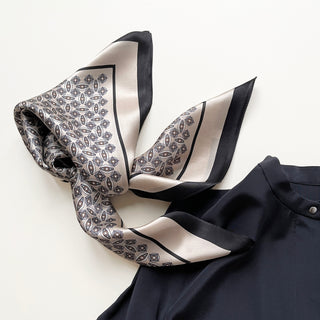 Black and silver silk bandana scarf with elegant geometric pattern, featuring diamond motifs and a contrasting black border, displayed with dark clothing