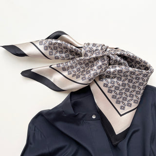 Elegant silk bandana scarf with champagne background and black geometric pattern, styled with black border, draped on navy shirt collar