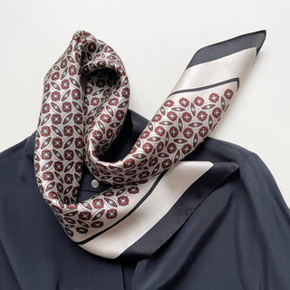 Silk bandana scarf with red and black geometric pattern, featuring intricate floral motifs on cream background with black border, styled on navy garment.