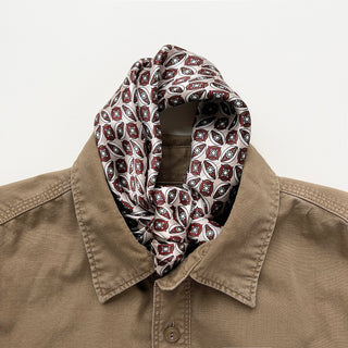 Silk bandana scarf with red and black geometric pattern styled inside collar of tan shirt, showcasing intricate diamond motifs