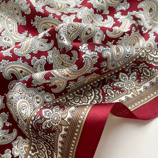 Luxurious dark red silk neckerchief with intricate beige and off-white paisley pattern, featuring elegant geometric border details and glossy fabric texture.