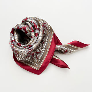 Luxurious dark red silk neckerchief with intricate beige and white paisley pattern, elegantly folded to showcase its geometric border and smooth finish