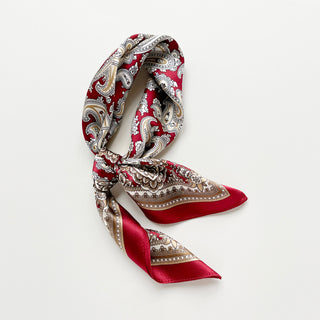 Luxurious dark red silk neckerchief with intricate beige and white paisley pattern, elegantly folded to display its silky texture and decorative border.