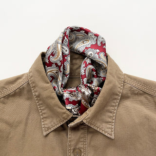 Dark red silk neckerchief with beige and white paisley pattern elegantly styled around collar of tan button-up shirt