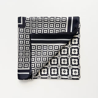 Elegant black and white silk scarf with geometric floral pattern, featuring hand-rolled edges and stylish border design, folded neatly.