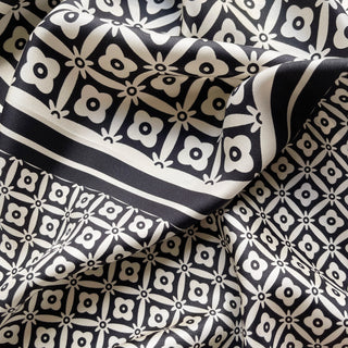 Luxurious black and white silk scarf with geometric floral pattern, featuring elegant hand-rolled edges and smooth fabric texture