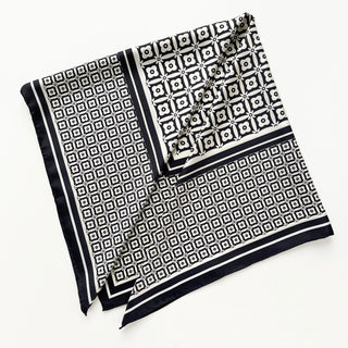 Elegant black and white silk scarf with geometric floral pattern, featuring hand-rolled edges and a classic border design on luxurious fabric
