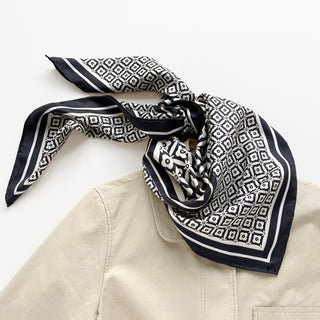 Luxury black and white silk scarf with geometric floral pattern and hand-rolled edges, elegantly draped on a beige garment