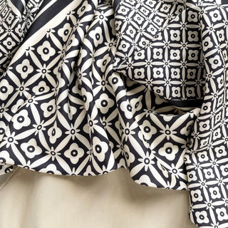Luxurious silk scarf with elegant black and white geometric floral pattern, showing detailed hand-rolled edges and silky texture in soft folds