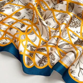 Luxurious silk scarf with botanical sketches on ivory background, gold baroque ribbon pattern, and teal border, elegantly draped to show texture