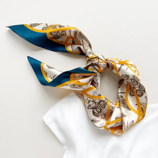 Luxury silk scarf with botanical illustrations and golden ribbon pattern on ivory backdrop, bordered with teal edges, tied in elegant knot