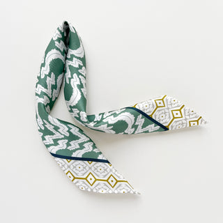 Teal green silk scarf with zigzag pattern and geometric white border featuring gold accents, displayed unfolded on white background
