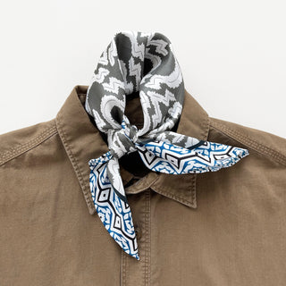 Silk scarf with teal and gray geometric pattern tied in a neckerchief style around a tan shirt collar, showcasing its versatile bandana design