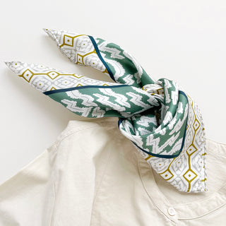 Teal green and white silk scarf with diamond geometric pattern and zigzag design, styled as a neck bandana on cream shirt collar