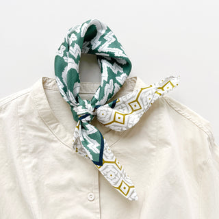 Teal green diamond grove silk scarf tied loosely around collar of cream shirt, showcasing geometric zigzag pattern and hand-rolled edges