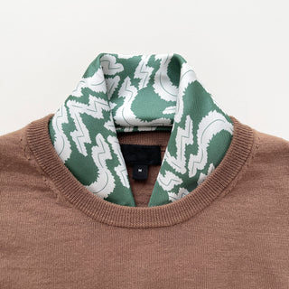 Teal green and white geometric pattern silk scarf elegantly styled with a brown sweater, showcasing its versatility as a luxury neck accessory.