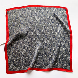Square silk neckerchief featuring blue and silver wave pattern with vibrant red border, showing the scarf's lustrous texture and elegant design