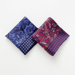 Two silk neckerchiefs featuring classic paisley patterns - one in plum red and one in navy blue, both with decorative floral borders and hand-rolled edges