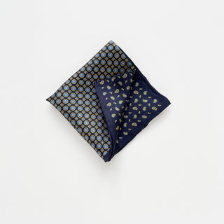 Navy blue silk pocket square with geometric circular patterns and paisley motifs, folded to display multiple design sections and hand-rolled edges