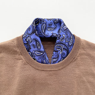 Blue silk paisley neckerchief styled with a tan sweater, showing elegant hand-rolled edges and classic pattern detail.