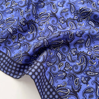 Luxurious blue silk neckerchief with classic paisley pattern, featuring intricate white detailing and navy border with small floral trim.