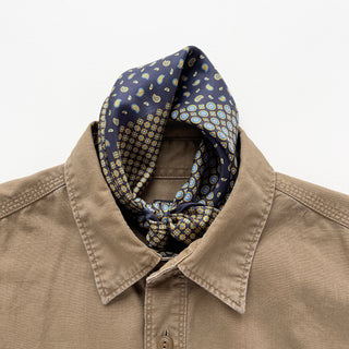 Navy blue silk neckerchief with paisley and geometric patterns styled in a knot around collar of beige shirt, showcasing luxurious texture