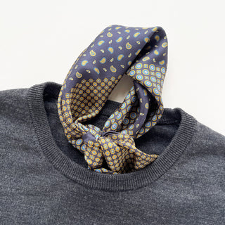 Navy blue silk neckerchief with paisley and geometric patterns in yellow and light blue, elegantly knotted over a gray sweater