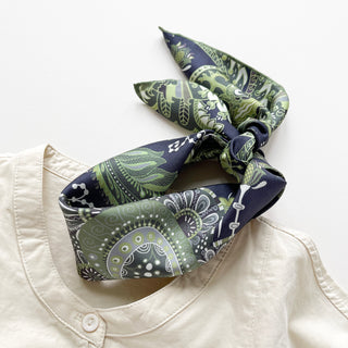 Forest green and navy silk scarf with intricate paisley pattern tied elegantly around cream shirt collar, showing luxurious silk texture