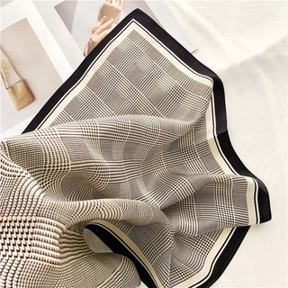 Elegant silk scarf with black houndstooth pattern on beige background, featuring black border trim, displayed with gentle folds showing luxurious texture
