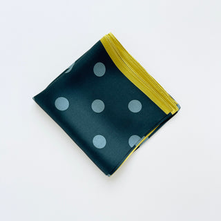 Square silk scarf with teal green background featuring light blue polka dots and vibrant mustard yellow border, folded neatly on white surface