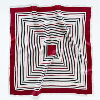 Square silk bandana featuring concentric geometric squares in red, navy, and off-white, with a rich red border and glossy silk finish.