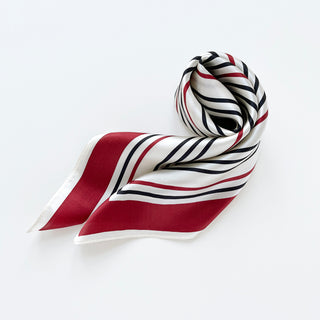 Square silk scarf with geometric striped pattern in red, navy and off-white, elegantly arranged to show its luxurious sheen and texture