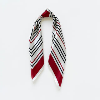 Square silk bandana scarf with geometric chevron pattern in red, navy and off-white, displayed draped to show its luxurious sheen and border detail.