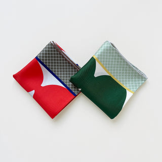 Two folded silk scarves - one orangey-red with grid pattern and white shapes, one deep green with geometric design and pale grid background