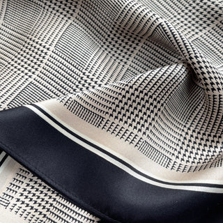 Elegant silk scarf with black houndstooth pattern on beige background, featuring black border trim, showing silky texture and luxurious drape