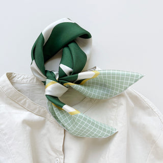 Silk scarf with deep green, white, and pale green grid pattern, elegantly tied at collar of cream blouse, showing refined texture and retro design