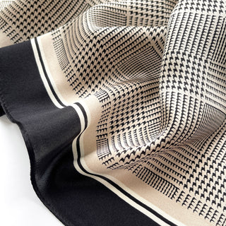 Elegant silk scarf with black houndstooth pattern on beige background, featuring black border with white stripes, displayed in soft folds