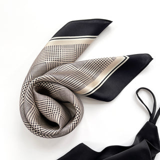 Elegant silk scarf with black houndstooth pattern on beige background, featuring solid black borders and delicate striped trim, displayed artfully draped