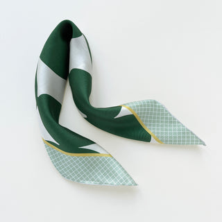 Square silk scarf with modern geometric design featuring deep green shapes on white background with light green checkered pattern and gold accent trim