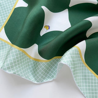 Luxurious silk scarf with deep green abstract pattern, white accents, mint grid border, and delicate yellow trim, featuring a small flower detail