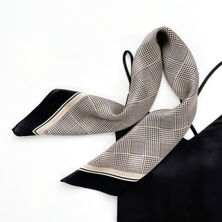 Elegant silk scarf with black houndstooth pattern on beige background, featuring black border trim, displayed in a softly draped style on white surface