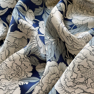 Luxurious blue silk scarf with elegant beige peony floral pattern, showing the fabric's delicate sheen and flowing texture