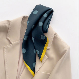 Teal green silk scarf with light blue polka dots and mustard yellow border, styled as a neck accessory on a beige blazer.